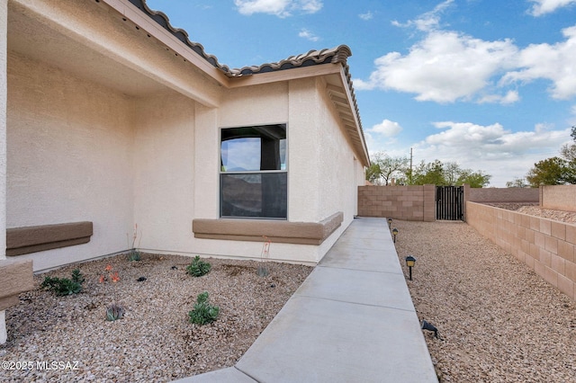 view of side of property with stucco siding, a gate, fence, and a tile roof