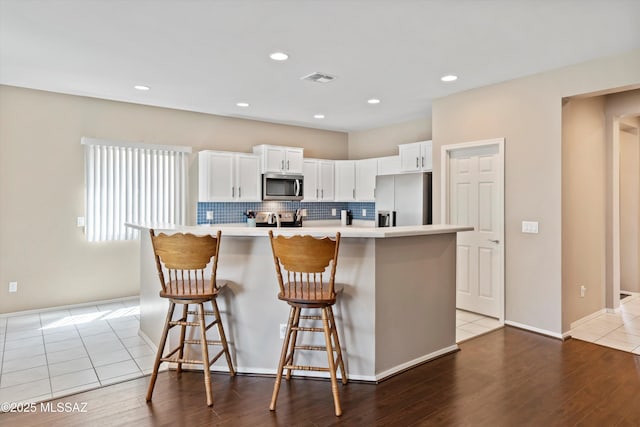 33743 S Ballad Dr, Red Rock, AZ 85145 - kitchen with a kitchen bar, white cabinetry, wood finished floors, stainless steel appliances, and decorative backsplash