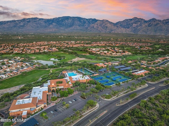 aerial view at dusk featuring a water and mountain view, golf course view, and a residential view