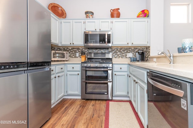 kitchen featuring a toaster, a sink, decorative backsplash, light countertops, and appliances with stainless steel finishes