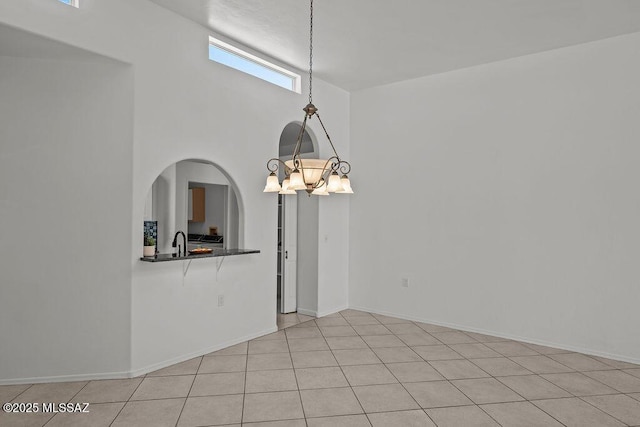 unfurnished dining area with an inviting chandelier, baseboards, arched walkways, and a sink