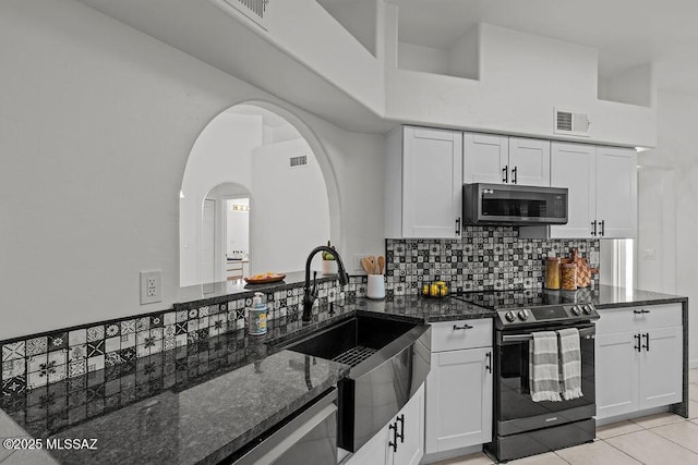 kitchen featuring dark stone countertops, stainless steel microwave, a sink, visible vents, and electric range oven