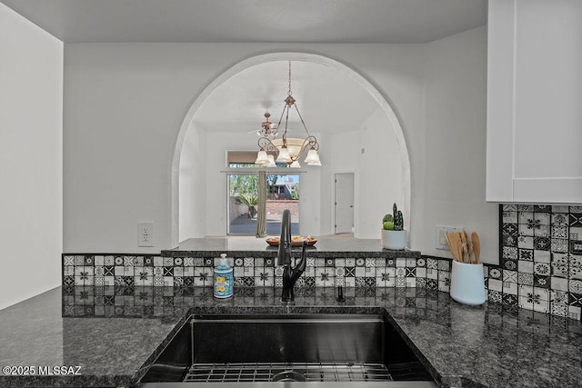 kitchen with a chandelier, decorative backsplash, arched walkways, and a sink