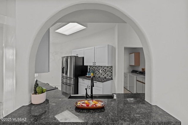 kitchen featuring independent washer and dryer, white cabinets, a sink, arched walkways, and stainless steel fridge with ice dispenser