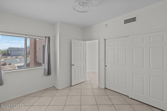 unfurnished bedroom featuring baseboards, visible vents, light tile patterned flooring, and a closet