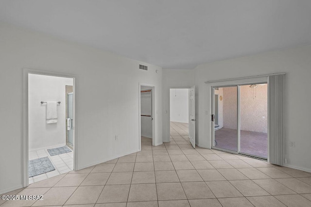 unfurnished bedroom featuring light tile patterned floors, access to outside, ensuite bath, a walk in closet, and visible vents