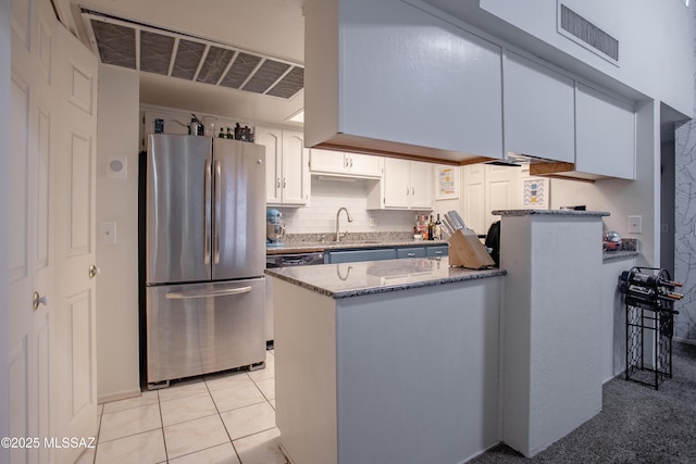 kitchen featuring white cabinetry, light stone counters, visible vents, freestanding refrigerator, and a peninsula