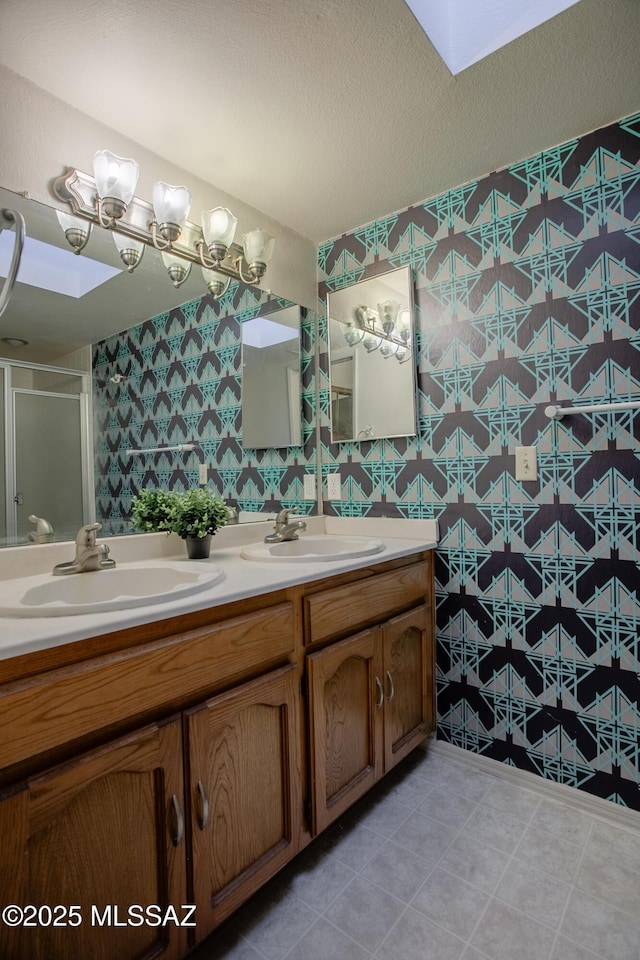 full bath featuring a shower stall, double vanity, wallpapered walls, and a sink