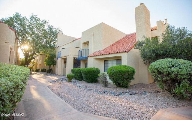 view of front of property featuring stucco siding, a chimney, a tile roof, and a balcony