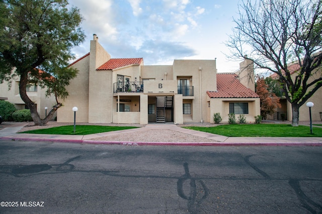 view of front of house with a tile roof, stucco siding, a balcony, a front lawn, and a chimney