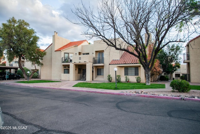 mediterranean / spanish home featuring stucco siding, a tile roof, a front lawn, and a balcony