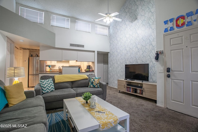 living room featuring a high ceiling, visible vents, dark colored carpet, and ceiling fan