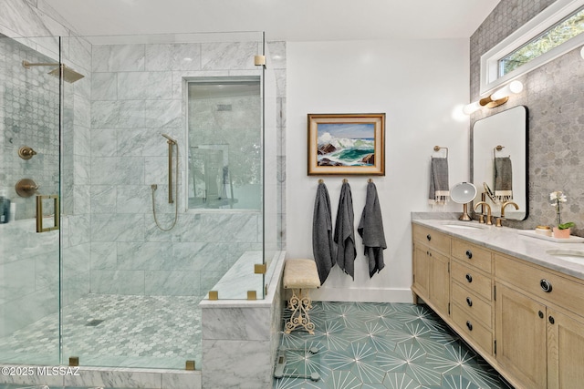 full bath with double vanity, tiled shower, baseboards, and a sink