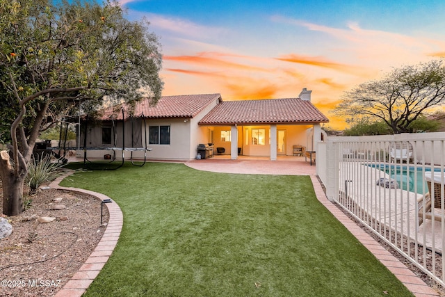 back of house with stucco siding, a tiled roof, a trampoline, a patio area, and a chimney