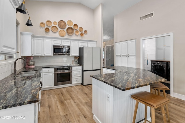kitchen featuring a sink, washing machine and clothes dryer, a kitchen bar, appliances with stainless steel finishes, and visible vents