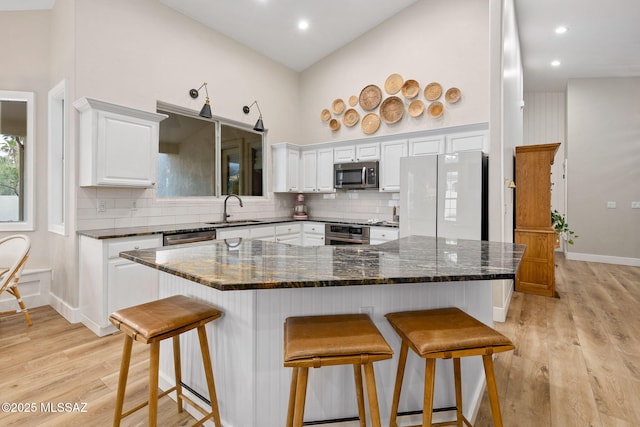 kitchen with a kitchen breakfast bar, white cabinets, a towering ceiling, and stainless steel appliances