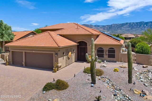 mediterranean / spanish-style house with a tile roof, decorative driveway, a mountain view, stucco siding, and a garage