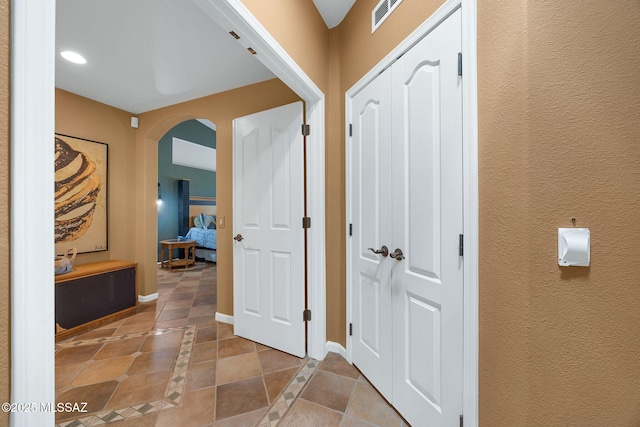 corridor with visible vents, a textured wall, baseboards, arched walkways, and tile patterned floors