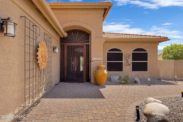 doorway to property featuring stucco siding, fence, and a tiled roof