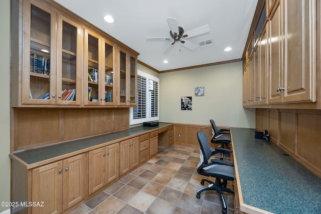 home office with crown molding, visible vents, ceiling fan, a wainscoted wall, and built in study area