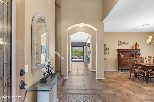 tiled foyer with arched walkways, a chandelier, and baseboards