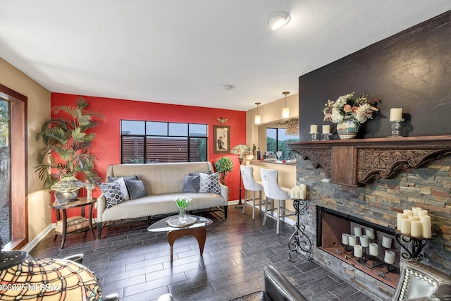 living room featuring a stone fireplace, a wealth of natural light, baseboards, and wood finish floors