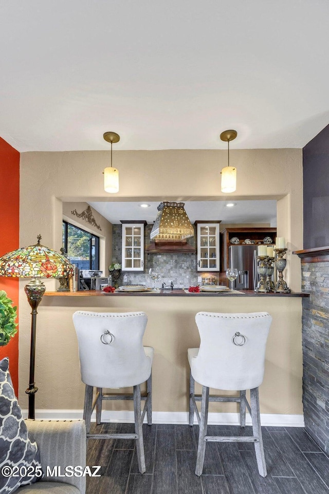 kitchen with stainless steel fridge with ice dispenser, glass insert cabinets, backsplash, and custom range hood