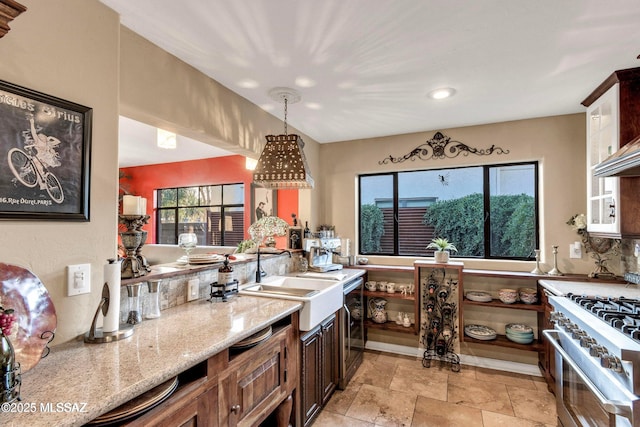 kitchen featuring high end stainless steel range oven, stone tile flooring, a sink, light stone counters, and pendant lighting