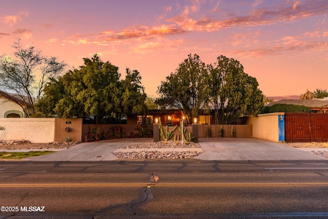 pueblo-style home with stucco siding, a gate, driveway, and a fenced front yard
