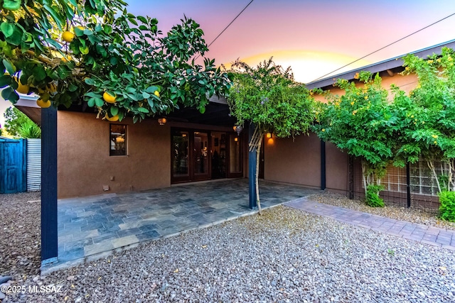 view of front of house featuring french doors, stucco siding, fence, and a patio