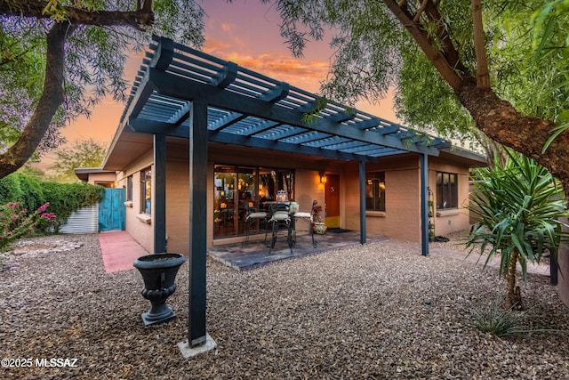 back of house at dusk featuring brick siding, a pergola, fence, and a patio