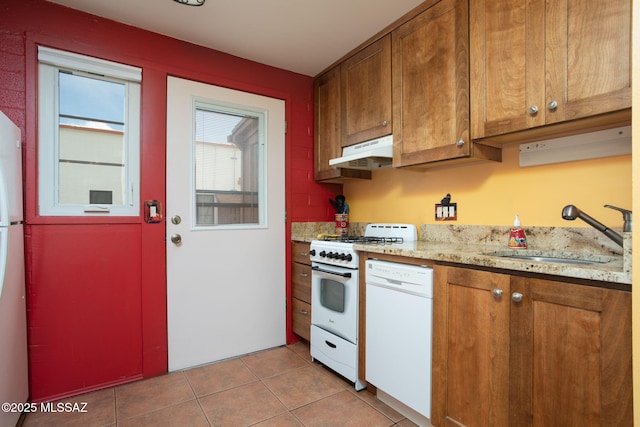 kitchen featuring light tile patterned flooring, white appliances, under cabinet range hood, a sink, and brown cabinetry