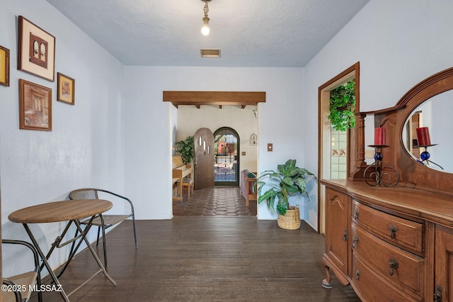 hallway featuring arched walkways, dark wood-style floors, a textured ceiling, and visible vents