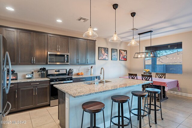 kitchen with visible vents, light stone countertops, stainless steel appliances, dark brown cabinets, and a sink