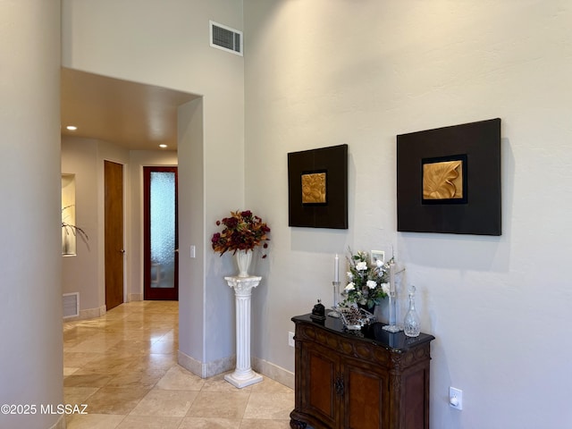 corridor featuring baseboards, visible vents, a high ceiling, and light tile patterned flooring
