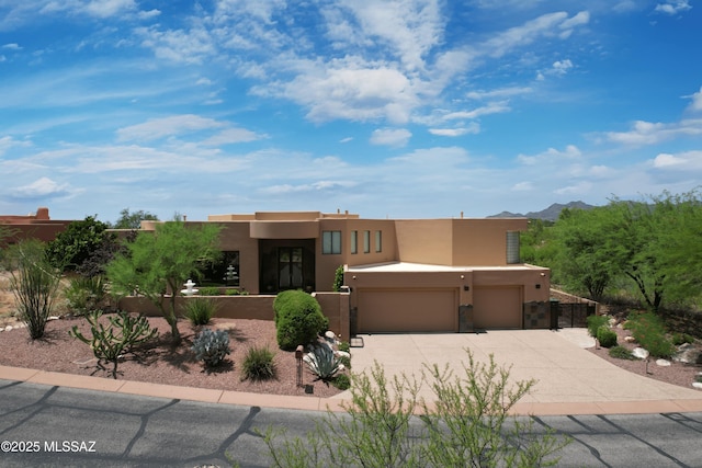 adobe home featuring stucco siding, fence, driveway, and an attached garage