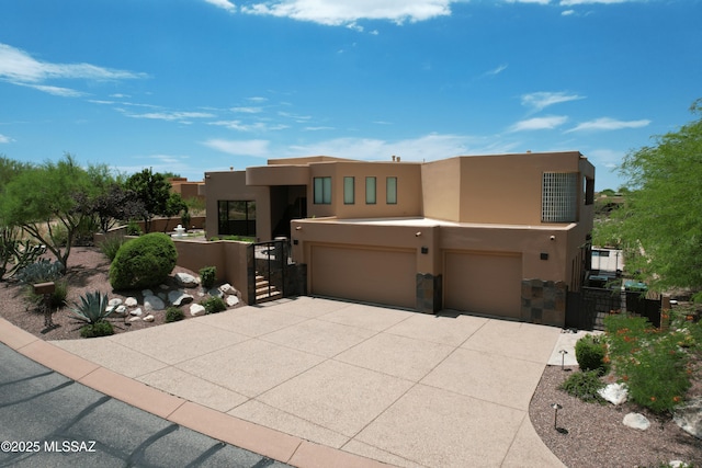 pueblo revival-style home with an attached garage, driveway, stucco siding, and a gate