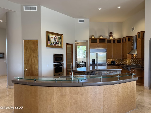 kitchen featuring wall chimney range hood, visible vents, stainless steel appliances, and a spacious island