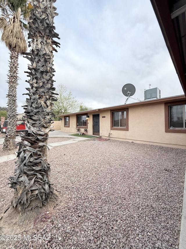 back of house with stucco siding and central air condition unit