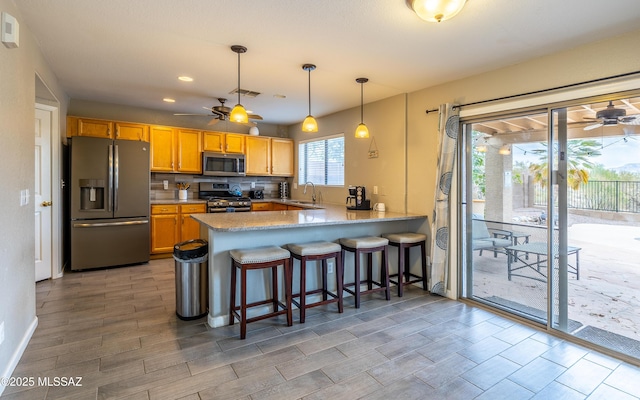 kitchen featuring a peninsula, a sink, a ceiling fan, and appliances with stainless steel finishes