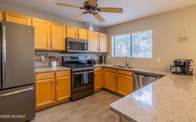 kitchen with a sink, a ceiling fan, tasteful backsplash, light wood-style flooring, and stainless steel appliances