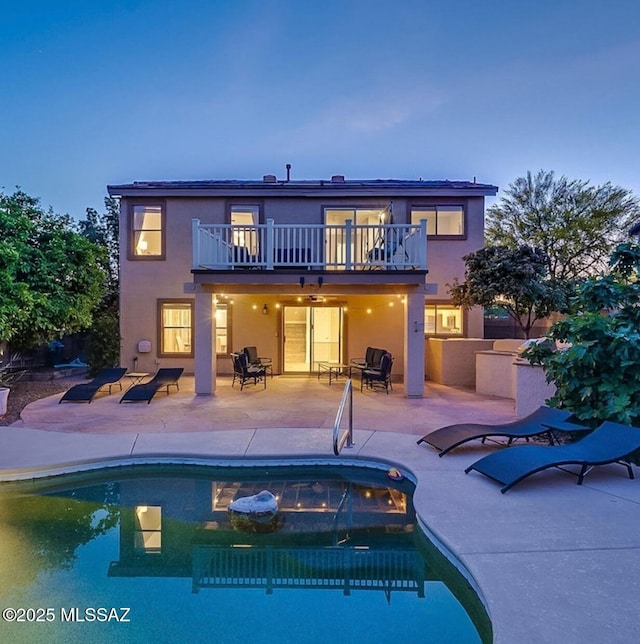 rear view of house with an outdoor pool, a balcony, stucco siding, and a patio