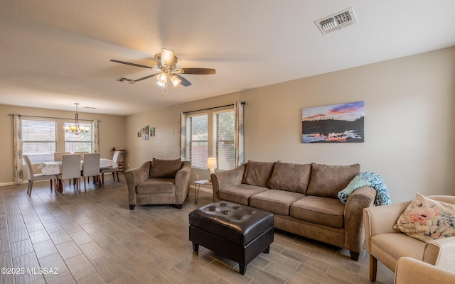 living area featuring a healthy amount of sunlight, visible vents, wood finish floors, and ceiling fan with notable chandelier