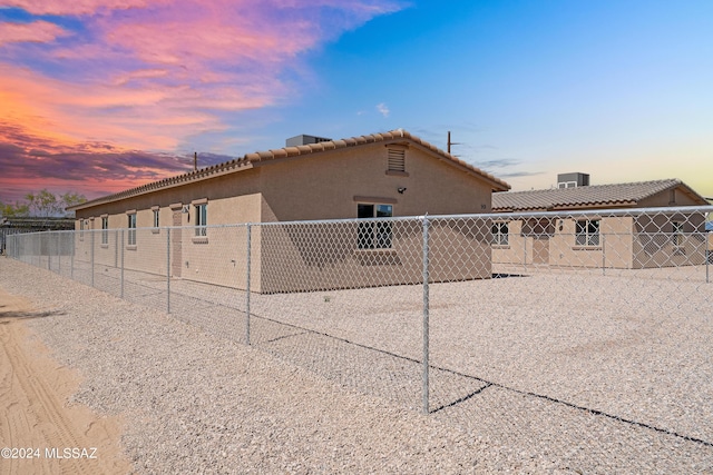 property exterior at dusk featuring a tile roof, stucco siding, and fence