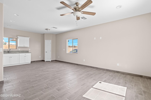 unfurnished living room featuring visible vents, light wood finished floors, baseboards, ceiling fan, and a sink