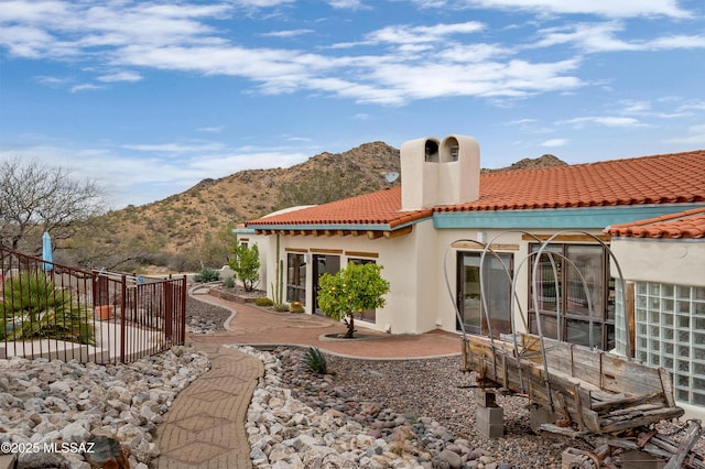 back of house featuring stucco siding, a mountain view, a chimney, a tiled roof, and fence