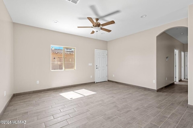 empty room with wood finished floors, arched walkways, baseboards, and ceiling fan