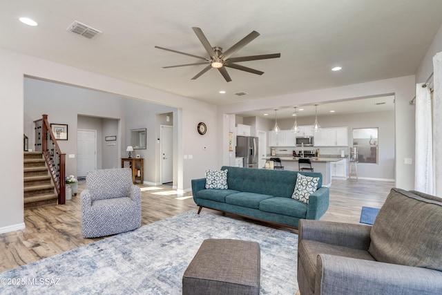 living room featuring ceiling fan, visible vents, baseboards, and light wood-style floors