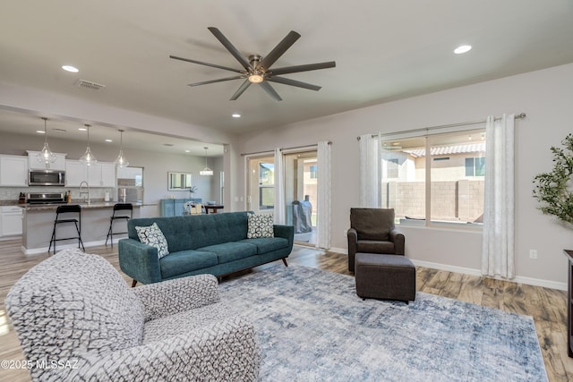 living room featuring visible vents, baseboards, recessed lighting, a ceiling fan, and light wood finished floors