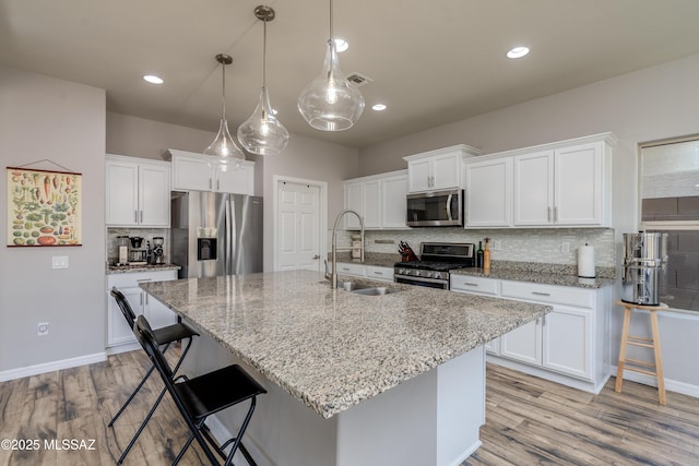 kitchen featuring visible vents, a center island with sink, tasteful backsplash, a sink, and appliances with stainless steel finishes